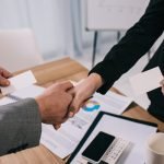 Cropped view of business partners shaking hands and giving visit cards to each other