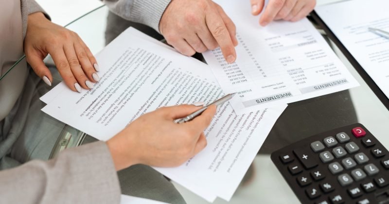 Hands of agent and mature man pointing at financial documents while discussing investments information